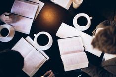 people are sitting at a table with open books and coffee mugs on top of it