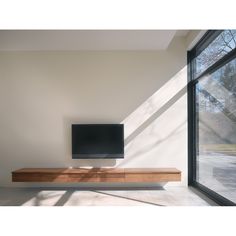 a flat screen tv sitting on top of a wooden shelf in front of a window