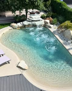 a small pool with a waterfall in the middle and lounge chairs on the other side