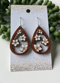 a pair of wooden earrings with white flowers in the shape of tears on top of a