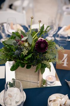 an arrangement of flowers and greenery in a wooden vase on a blue table cloth