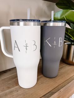 two personalized tumblers sitting on top of a wooden shelf next to a potted plant