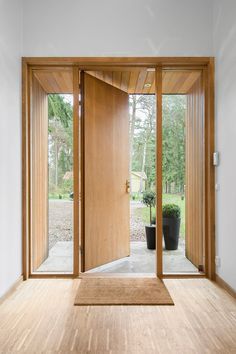 an open wooden door in the middle of a room with wood floors and large windows