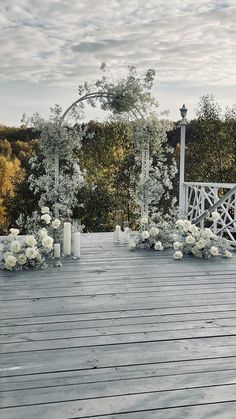 an outdoor wedding setup with white flowers and candles on the deck, surrounded by trees