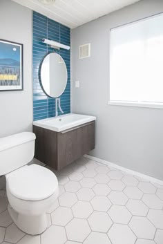 a white toilet sitting next to a bathroom sink under a mirror on top of a wooden cabinet