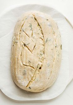 a piece of bread sitting on top of a white paper covered plate with cheese and herbs