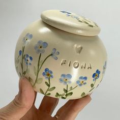 a hand holding a ceramic jar with flowers painted on it