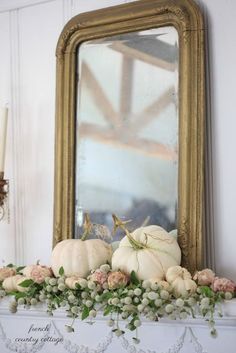 white pumpkins and greenery sit on a mantel in front of a mirror