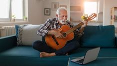 an older man sitting on a couch playing the guitar