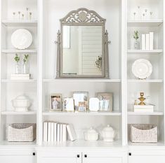 a white bookcase filled with lots of books next to a mirror and other items