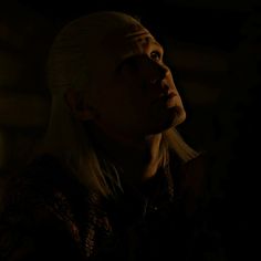 an older woman with white hair looking off into the distance in a dark room at night