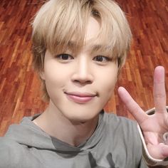 a young man making the peace sign with his hand while standing in front of a wooden floor