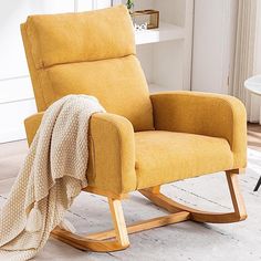 a yellow rocking chair with a blanket on top of it and a table in the background