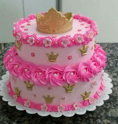 a three tiered cake with pink icing and gold crown on top, sitting on a table