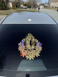 an image of the virgin mary in gold on a black car window with flowers and leaves