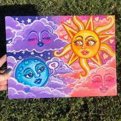 someone is holding up a painting on the grass with sun and moon faces painted on it