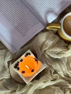 an open book on a bed next to a cup of coffee and a lit candle