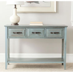 a blue console table with three drawers and a lamp on the sideboard next to it