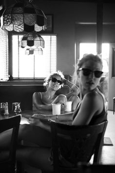 two women sitting at a table with cups in front of them and one woman wearing sunglasses