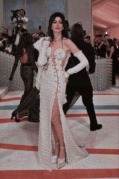 a woman in a white dress standing on a red and blue carpet with people behind her