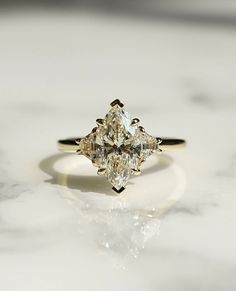 a three stone diamond ring sitting on top of a marble countertop in front of a white background