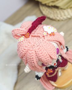 a small knitted doll wearing a pink hat and dress with flowers on it's head