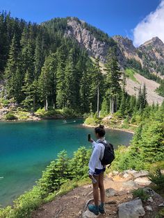 a person standing at the edge of a mountain looking out over a lake and forest