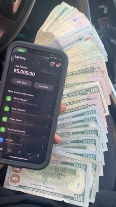 a person holding a cell phone with money in the background