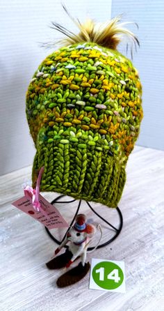 One-of-a-kind, ready-to-ship, handmade winter hat/beanie.  Bursting with color, this green, and mustard yellow multi-colored beanie features a 4" gold, faux fur, removable PomPom.  Made of fine Malabrigo Rasta wool yarn, this beanie must be hand washed and dried flat to preserve its softness and durability.  The hat measures 8" across and 9" tall allowing the wearer to pull it down over the ears or roll it up depending on the required warmth.  Knit from my own original design, The Poppy Hat pattern is available on Ravelry for the adventurous beginning knitter.  As with any handmade item, minor flaws and imperfections are inherent to its construction and adds a unique charm to the finished project. Whimsical Beanie For Winter, Whimsical One-size Beanie For Winter, Handmade One Size Beanie For Cold Weather, Handmade One-size Beanie For Cold Weather, Green Winter Hat For Cold Weather, Whimsical One Size Bonnet For Winter, Whimsical One-size Bonnet For Winter, Whimsical Winter Bonnet, One Size, Green Winter Cap Hat