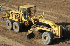 a large yellow bulldozer is parked in the middle of a dirt field with two men standing nearby