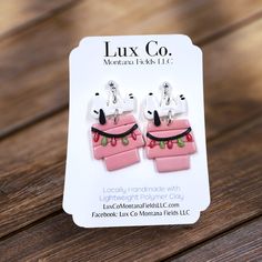 the earrings are pink and white with black accents on them, sitting on a wooden table