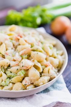 a white bowl filled with pasta salad next to green onions and celery sticks