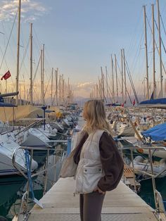 a woman is standing on a dock in front of many sailboats and boats at sunset