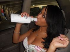 a woman sitting in the back seat of a car drinking from a white bottle while wearing a dress