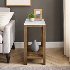 a small table with a vase on it in front of a couch and framed pictures