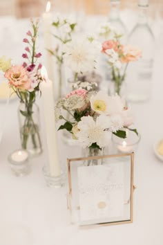 there are flowers in vases on the table with candles and cards for guests to sign