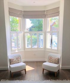 two white chairs sitting in front of a window with shutters on the windowsill