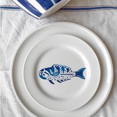 a white plate with blue fish painted on it and a bowl next to the plate