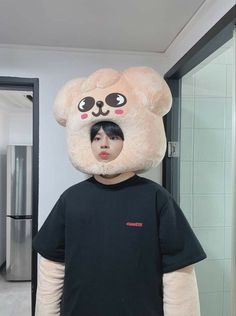 a person wearing a large teddy bear head and black shirt standing in front of a mirror