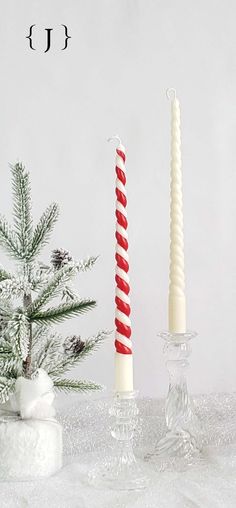 two candles sitting on top of a table next to a small christmas tree in a vase