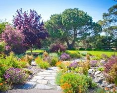 a garden with flowers and trees in the background, along with a stone path that leads to a grassy area