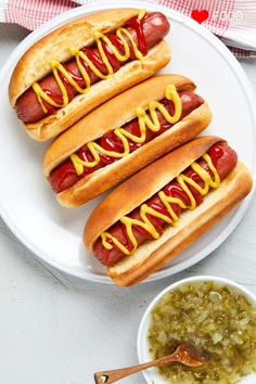 two hotdogs with mustard and ketchup on a plate next to a bowl of relish