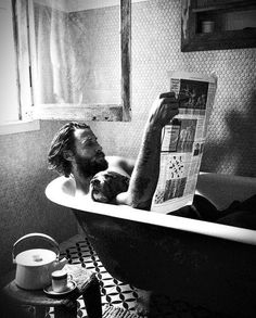 a man laying in a bathtub reading a newspaper