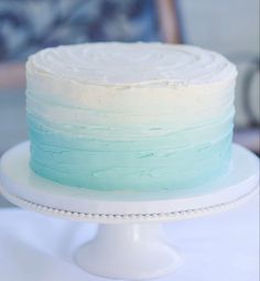 a white cake with blue frosting sitting on top of a table next to a plate