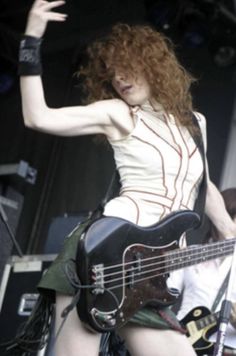 a woman with long red hair is playing the bass guitar on stage at a music festival