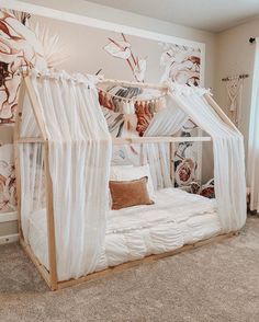 a canopy bed with curtains and pillows in a room that has carpet on the floor