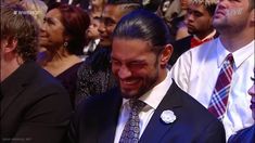 a man in a suit and tie smiles as he sits next to other people at an event