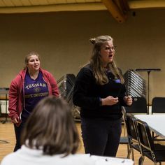 two women standing next to each other in front of a group of people on a wooden floor