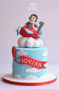 a blue and red cake with a boy sitting on top of it, in the shape of an airplane