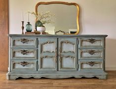 an old blue dresser with mirror and vases on the top, in front of a wooden floor